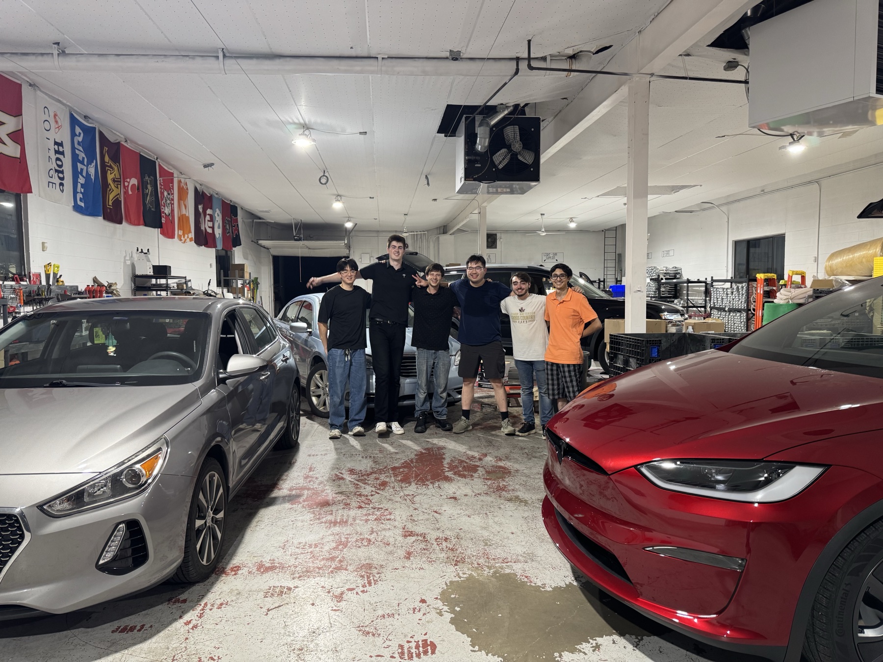 Six Midwest EV team members together in their repair workshop, with cars and tools around them